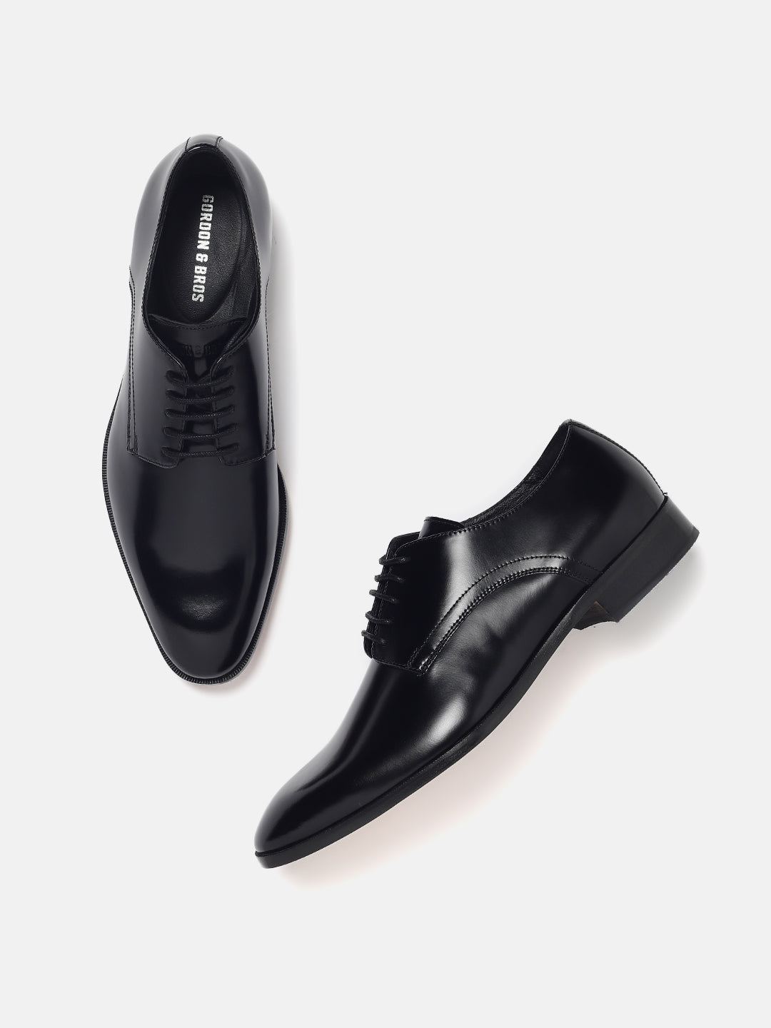 A pair of black lace-up derby shoes on a white background.