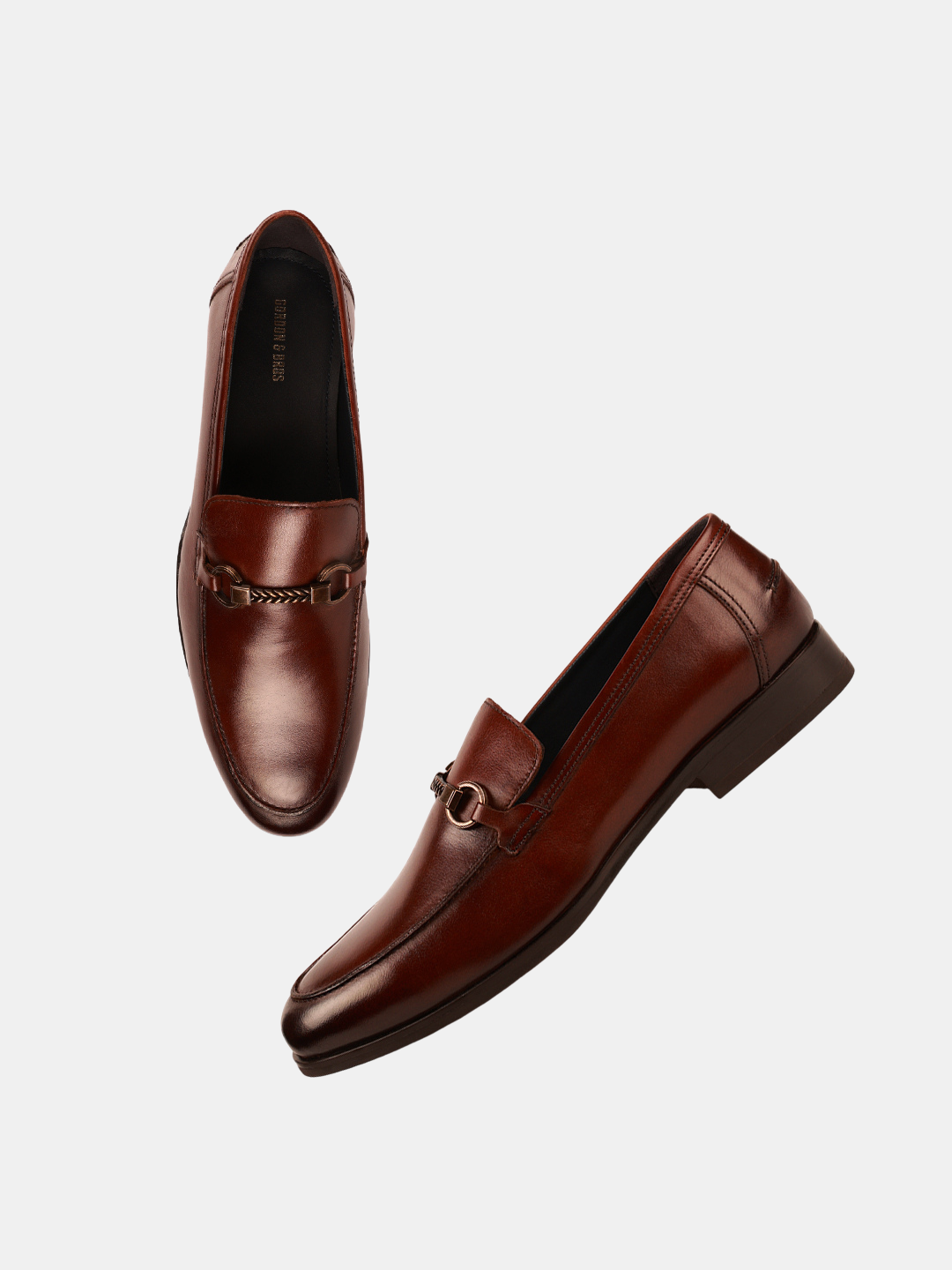 A pair of brown leather loafers with a metal buckle strap, isolated on a white background.